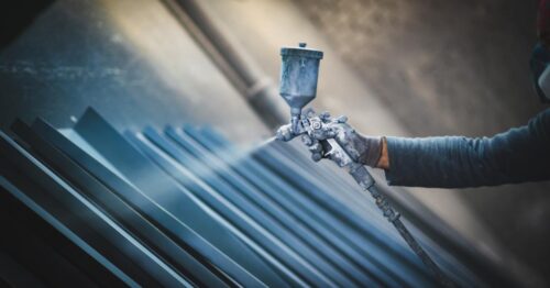A close-up of a worker activating a spray gun to powder coat a series of aluminum sheets in grey color.
