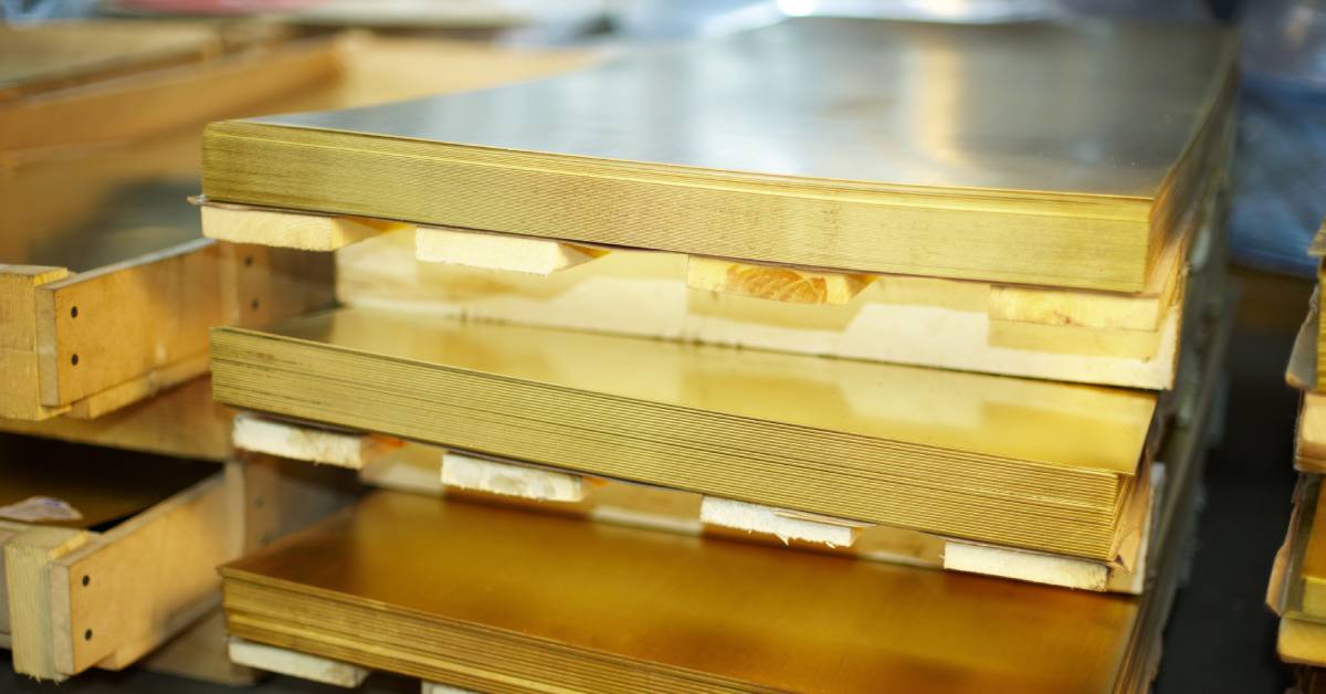 A stack of brass sheet plates sitting on warehouse pallets. The light reflects off the surface of the top sheet.