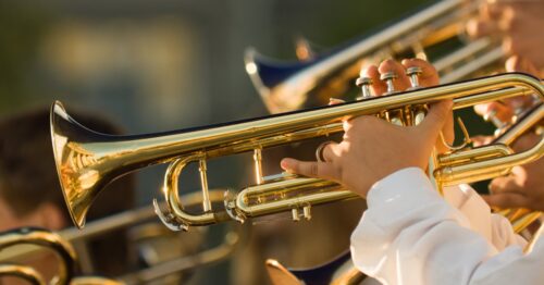 A person wearing a white shirt holds a brass trumpet. Other trumpet players are next to this person.
