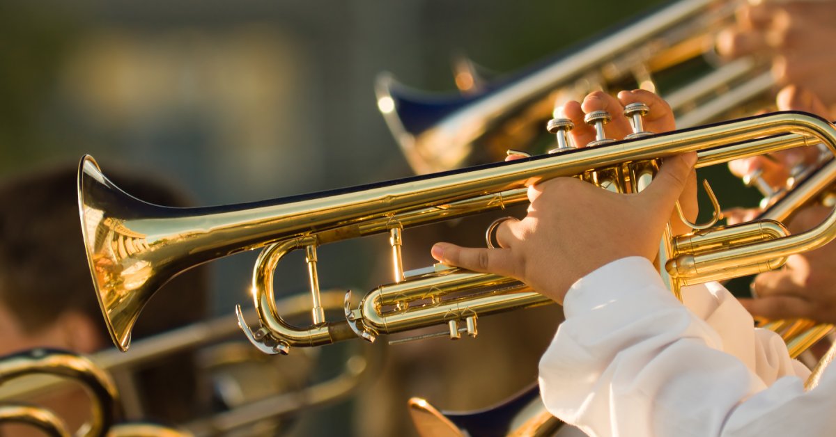 A person wearing a white shirt holds a brass trumpet. Other trumpet players are next to this person.