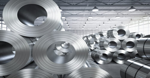A roll of stainless steel sheets sits stacked inside a factory. The sheets shine under the factory lights.