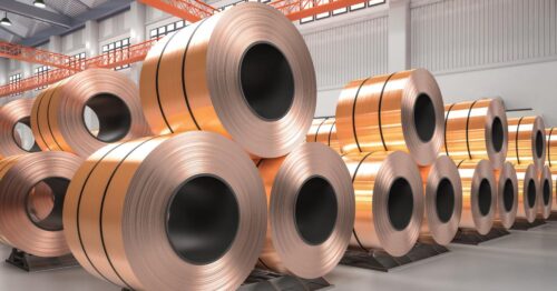 Large copper coils neatly stacked in an industrial warehouse with bright overhead beams and modern storage racks.