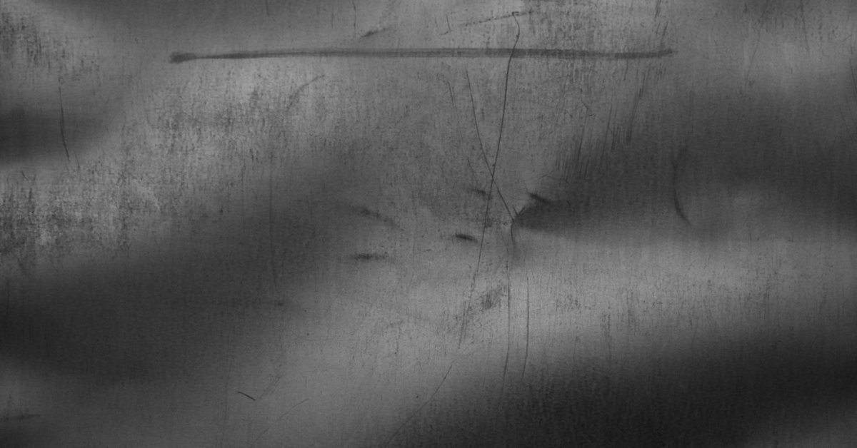 A close up view of some sheet metal. The metal surface has a few scratches across it and a dent in the middle.