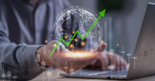 A man on his laptop with one hand in a cupped position. In it is a graphic of a globe with a stock arrow rising through it.