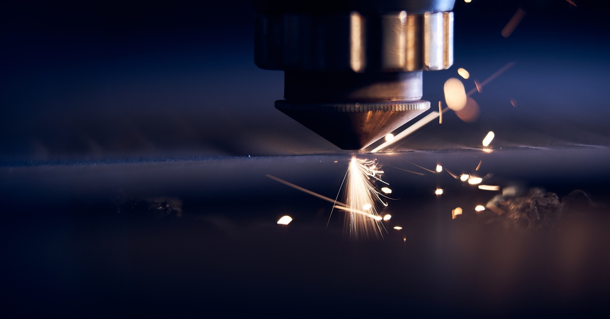 A CNC laser cutting metal at close range, with bright sparks coming off of it. The metal sheet looks relatively clean.