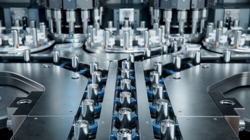 Rows of cylindrical battery cells arranged on a conveyor inside an automated industrial production line.