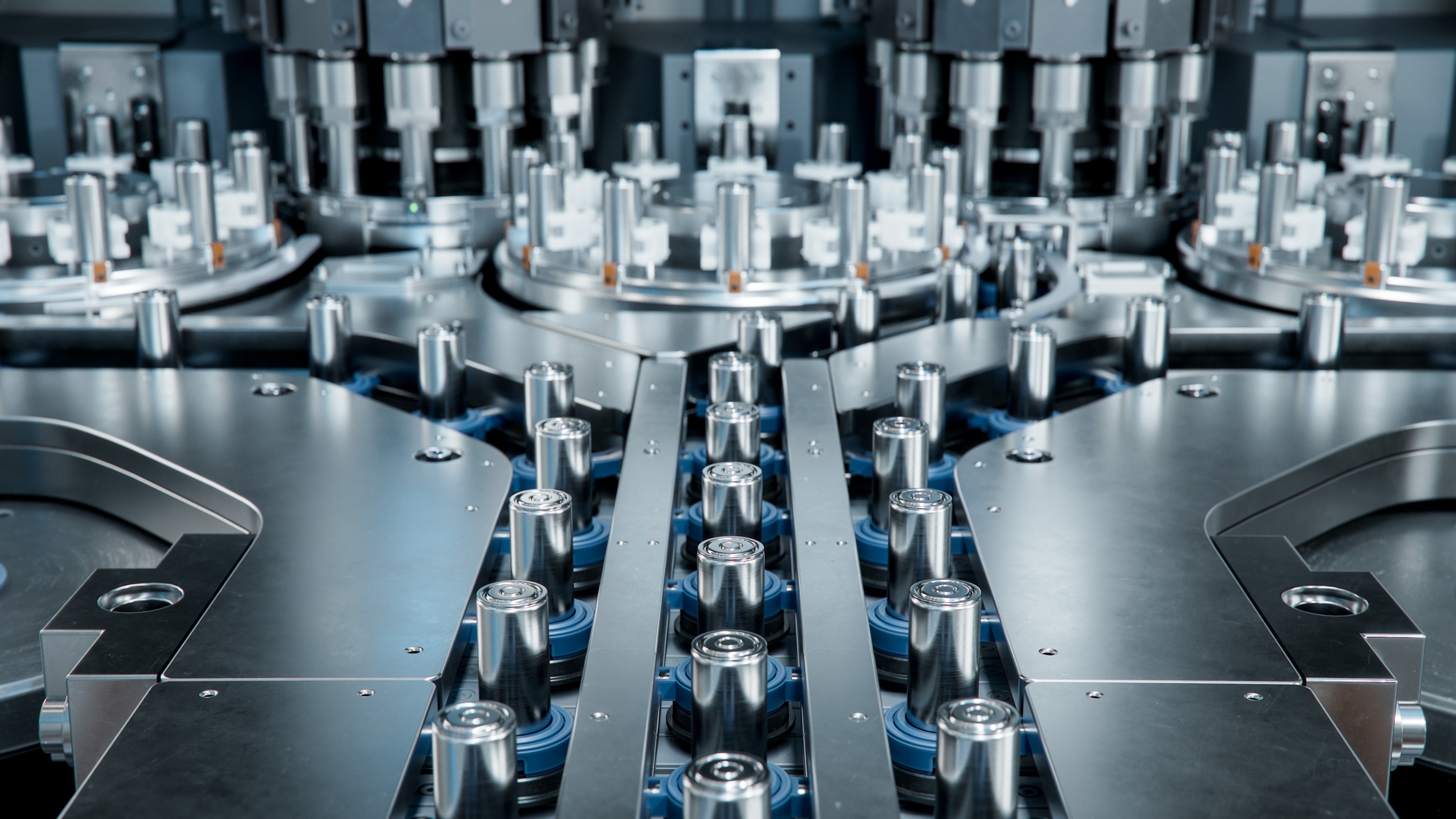 Rows of cylindrical battery cells arranged on a conveyor inside an automated industrial production line.