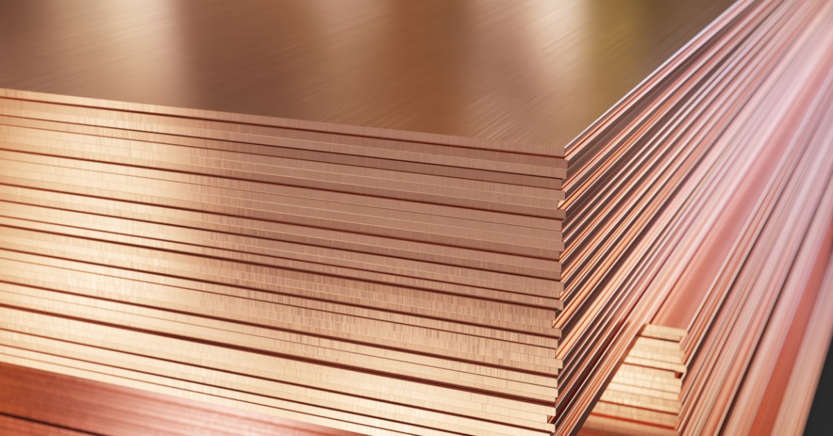 A close-up view of copper sheets stacked in a warehouse, showing smooth reflective surfaces and rough metal edges.